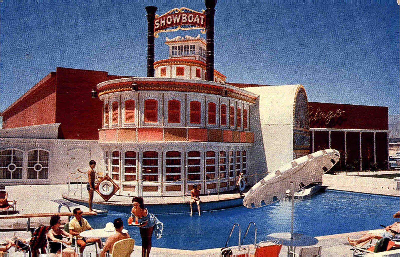 1961 color postcard view of the Showboat's swimming pool with the white riverboat facade behind it, twin black smokestacks, a lit SHOWBOAT sign, yellow Bingo neon script on the red casino block, and guests lounging poolside