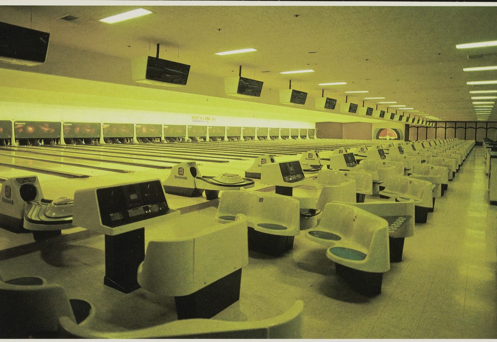 A late-1970s postcard photograph of the Showboat bowling center: rows of molded seating and Brunswick ball returns in the foreground, automatic scoring consoles, overhead monitors, and dozens of lanes receding to the pin decks