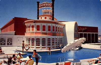 1961 color postcard view of the Showboat's swimming pool with the white riverboat facade behind it, twin black smokestacks, a lit SHOWBOAT sign, yellow Bingo neon script on the red casino block, and guests lounging poolside