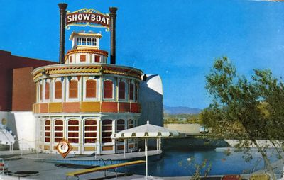 A 1950s color postcard view of the Showboat's round riverboat prow with its SHOWBOAT sign and twin smokestacks rising over the swimming pool, a white parasol and diving board at the water's edge